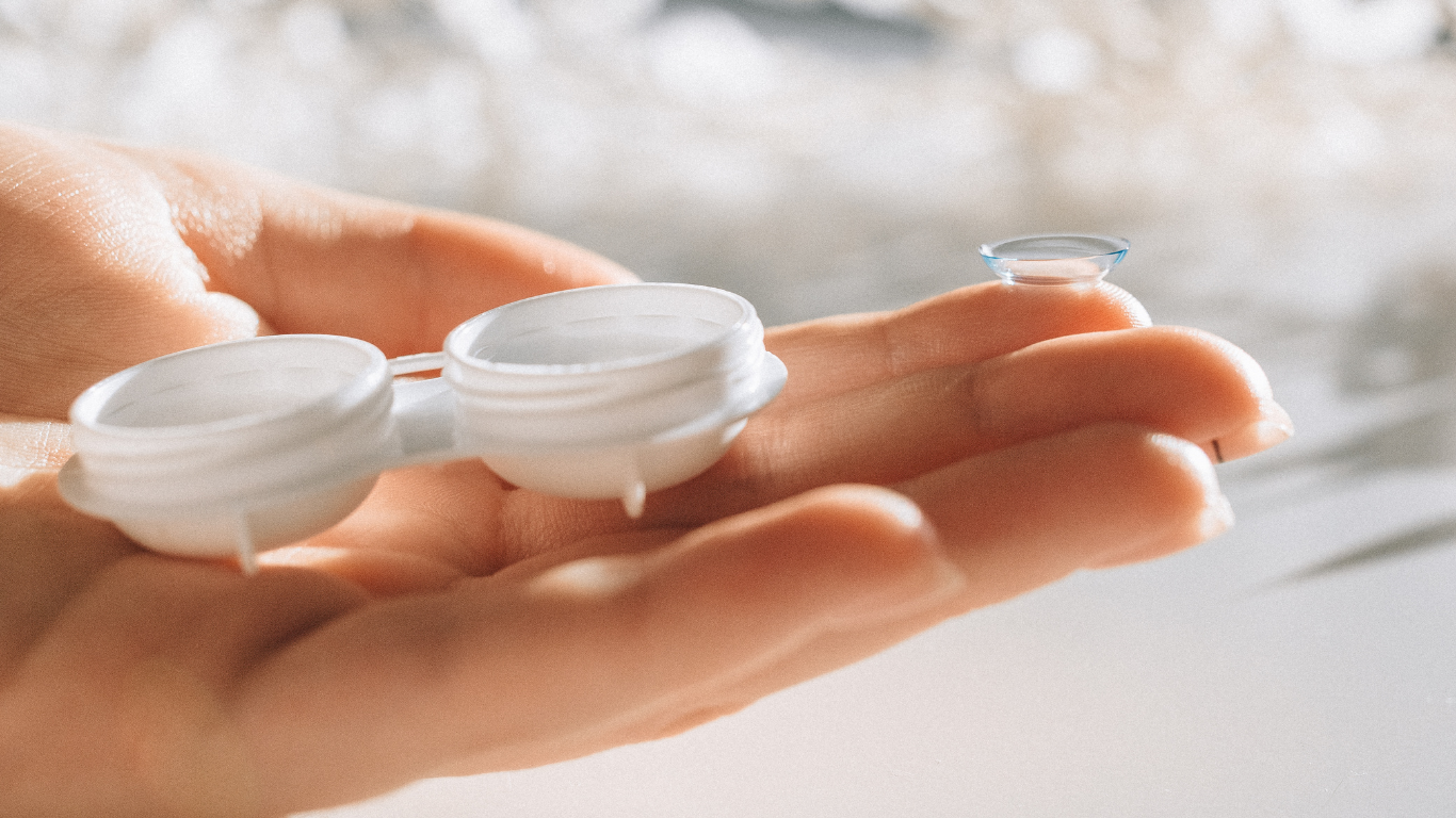 Close-up of a hand holding a contact lens case with a small, transparent contact lens on the fingertip.