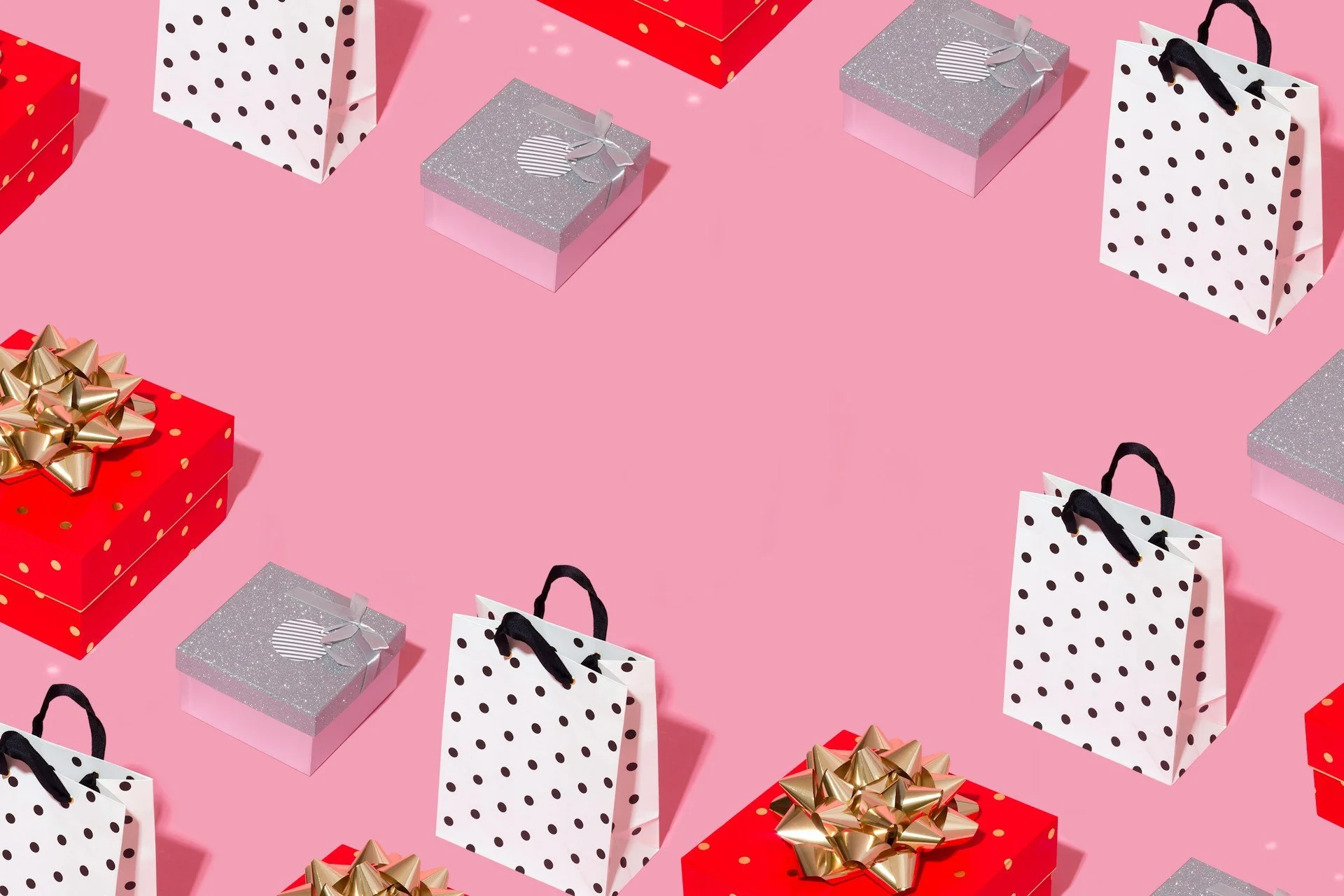 Multiple gift boxes and shopping bags on a pink background, with red and silver presents, some decorated with bows.