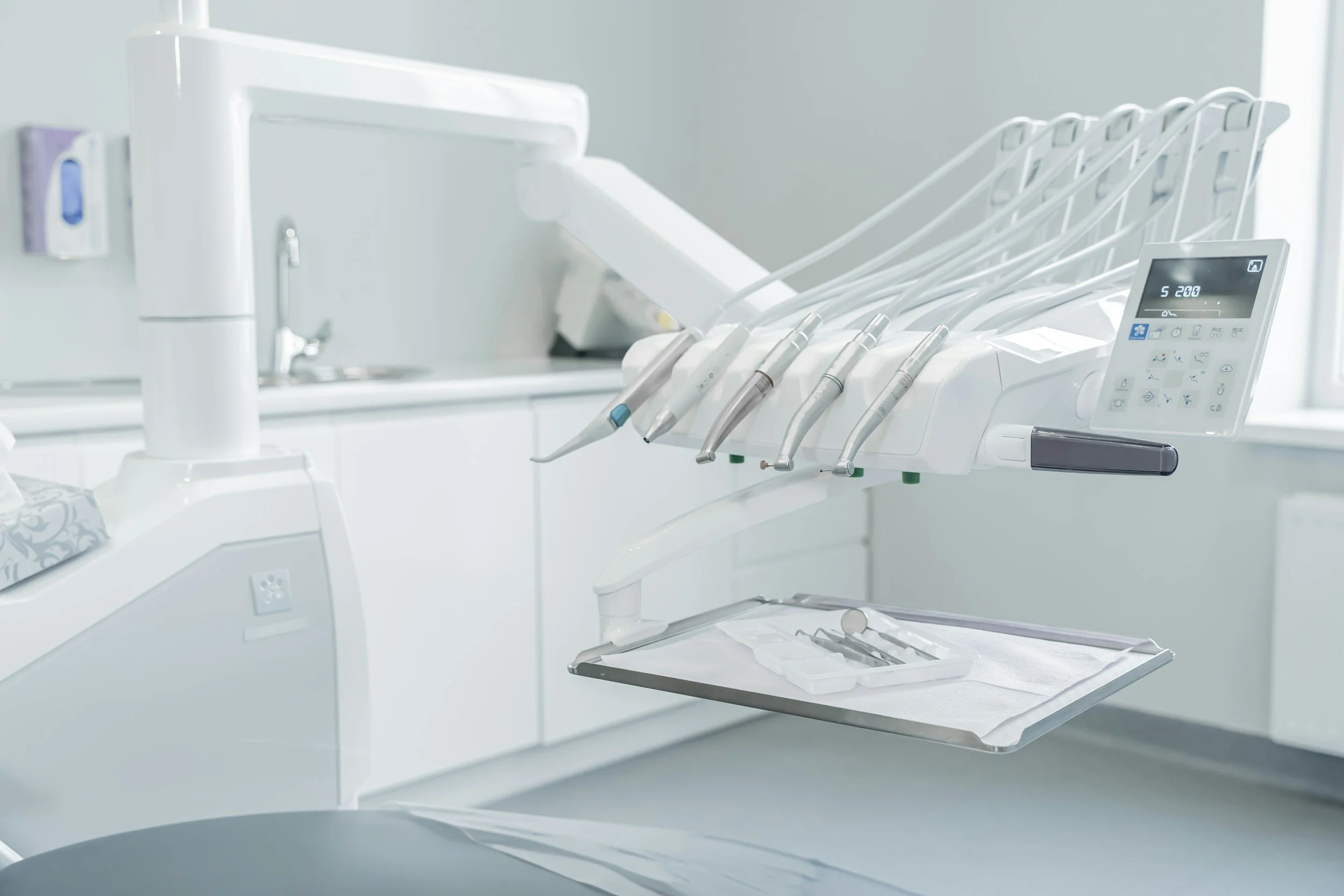 Dental instruments arranged on a tray in a dental office with a dental drill, suction, and other tools, and a digital control panel.