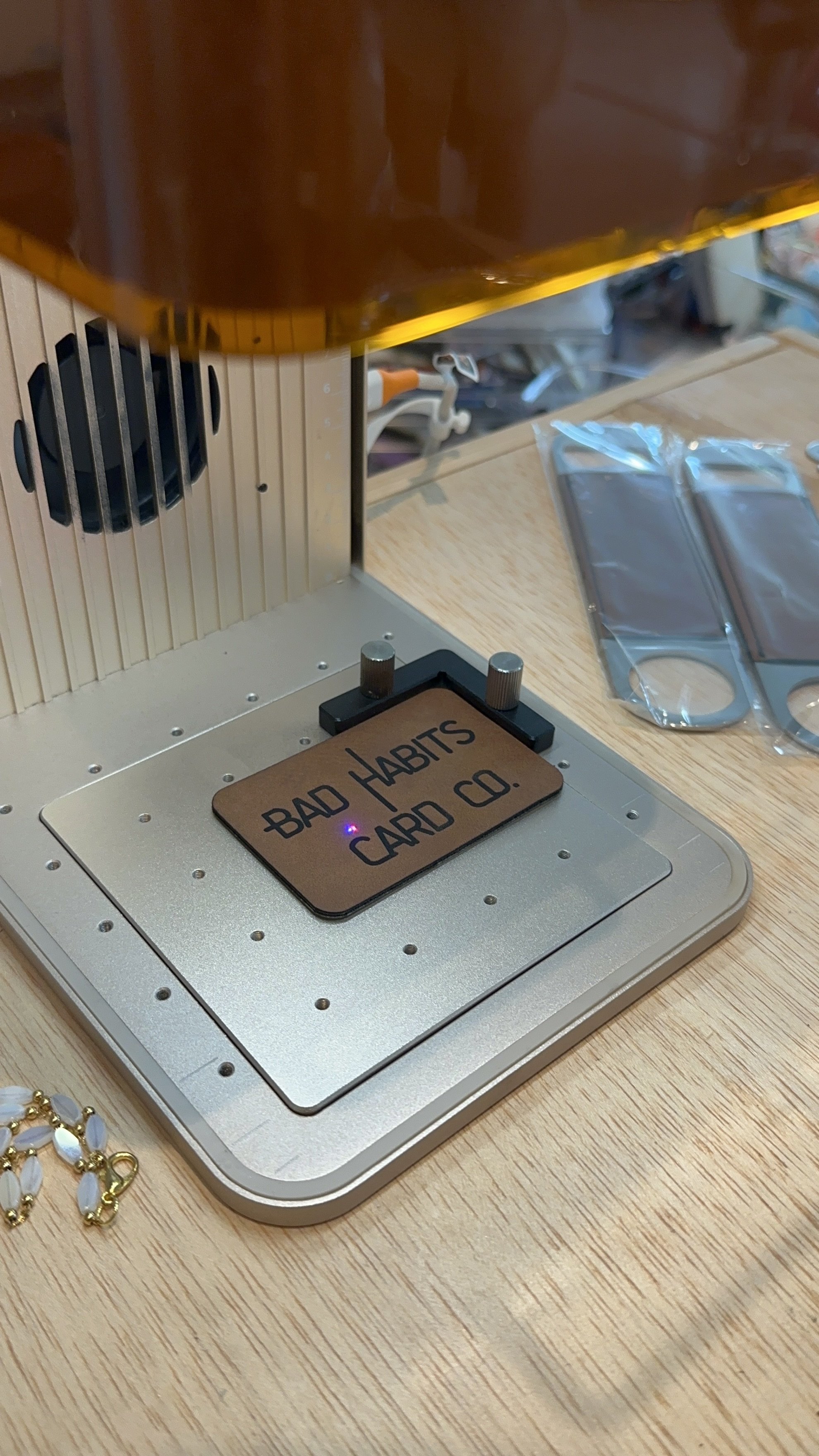 A metal switch with a sign reading 'BAD HABITS CARD CO.' on top. The switch is on a wooden table, with some jewelry and plastic-wrapped items nearby.