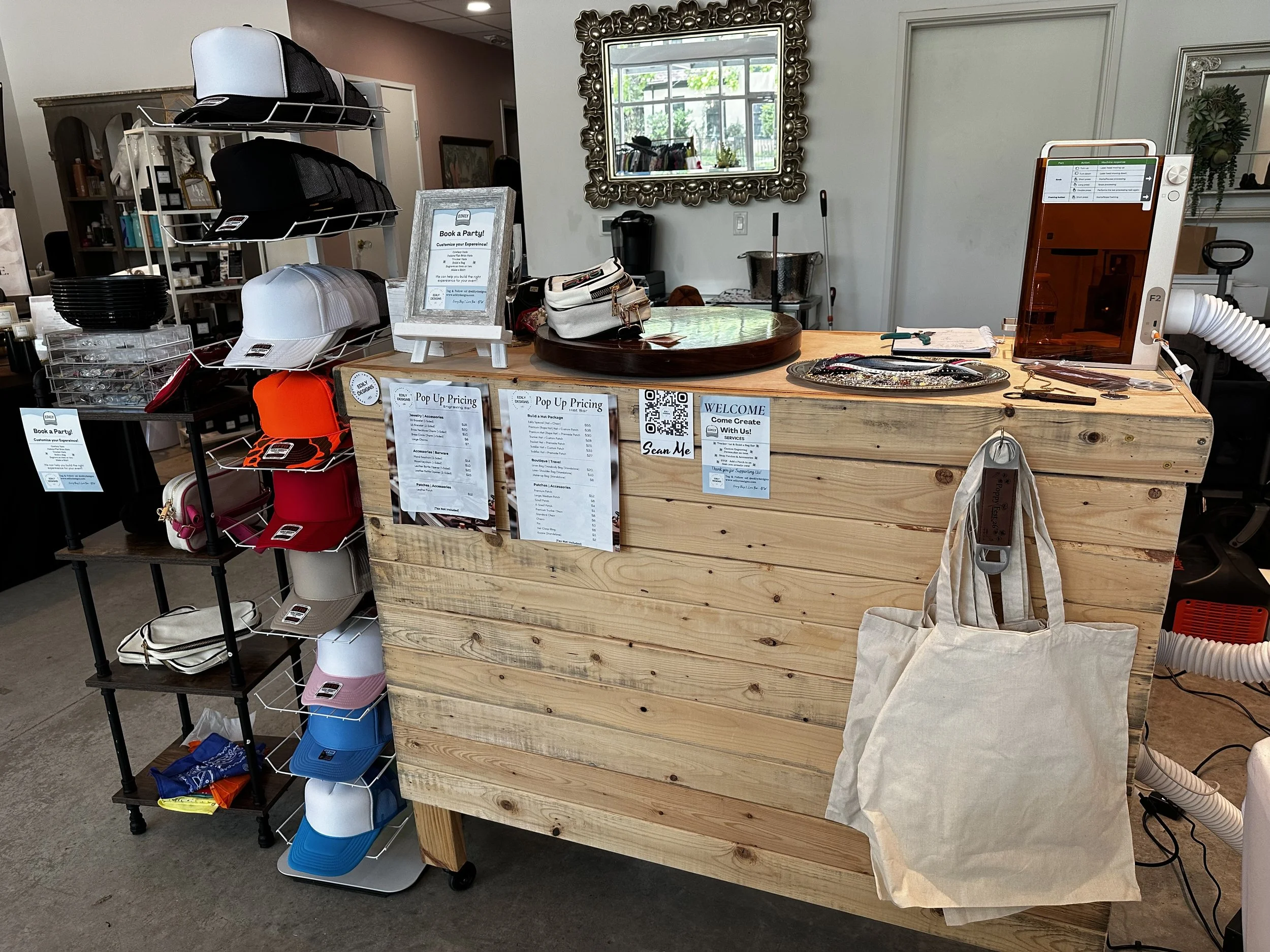 A display table with hats and accessories next to a larger wooden counter with a virtual tanning machine. The background includes a mirror, some shelves, and a window.