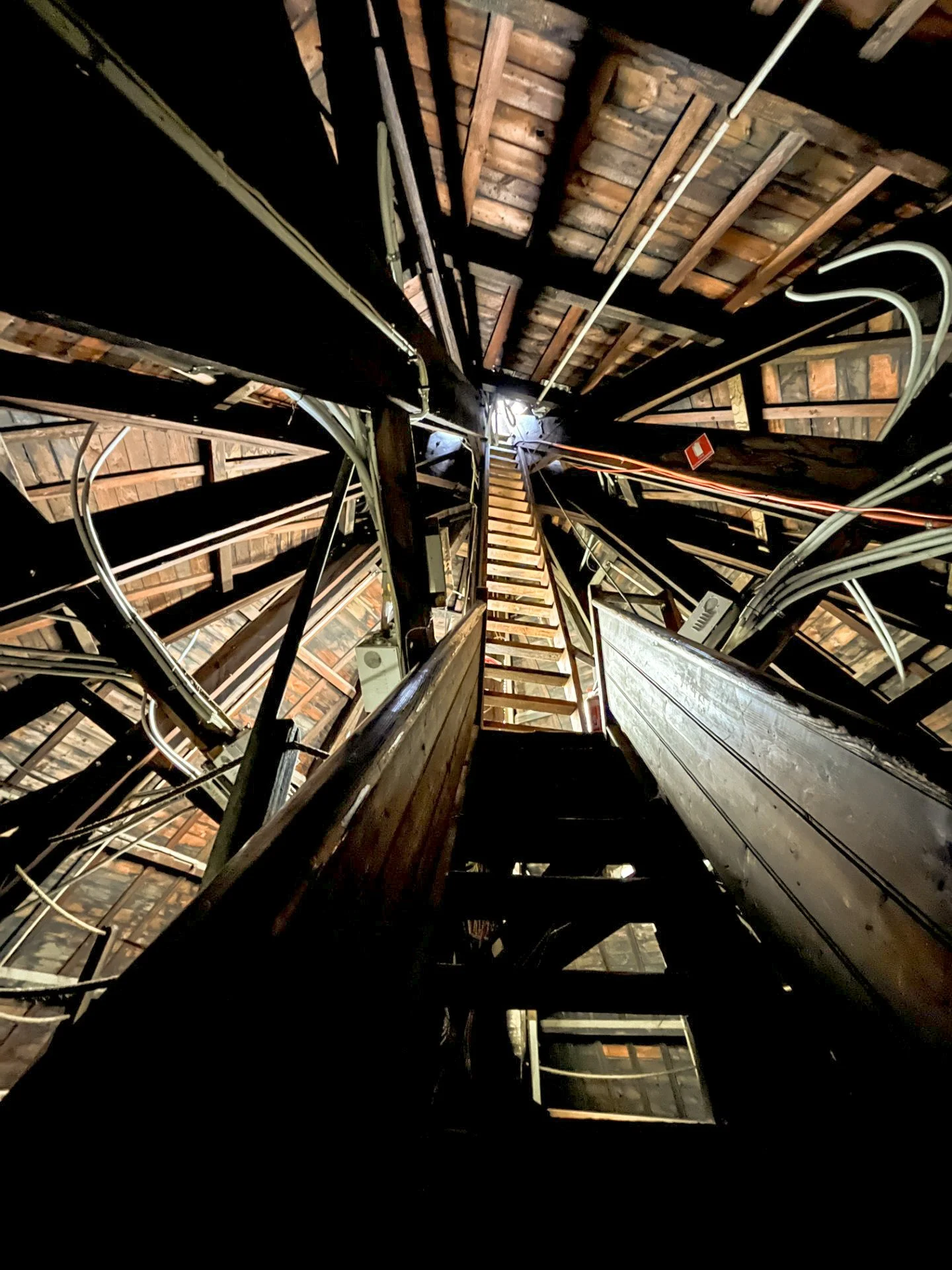 Looking up inside a wooden tower with a ladder and exposed electrical wiring, beams, and insulation.