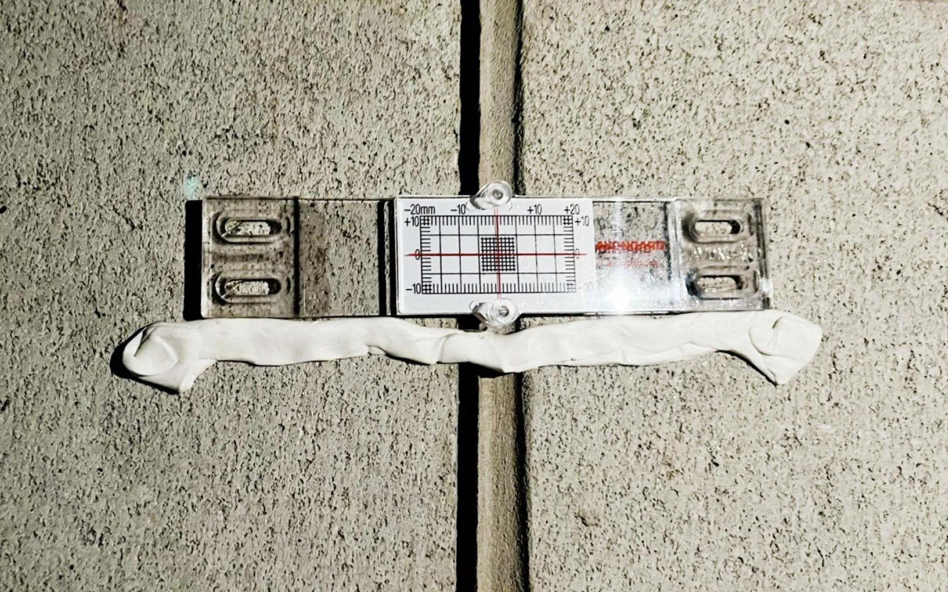 A laser level tool positioned on a tiled wall to check the straightness of the joint between two tiles.
