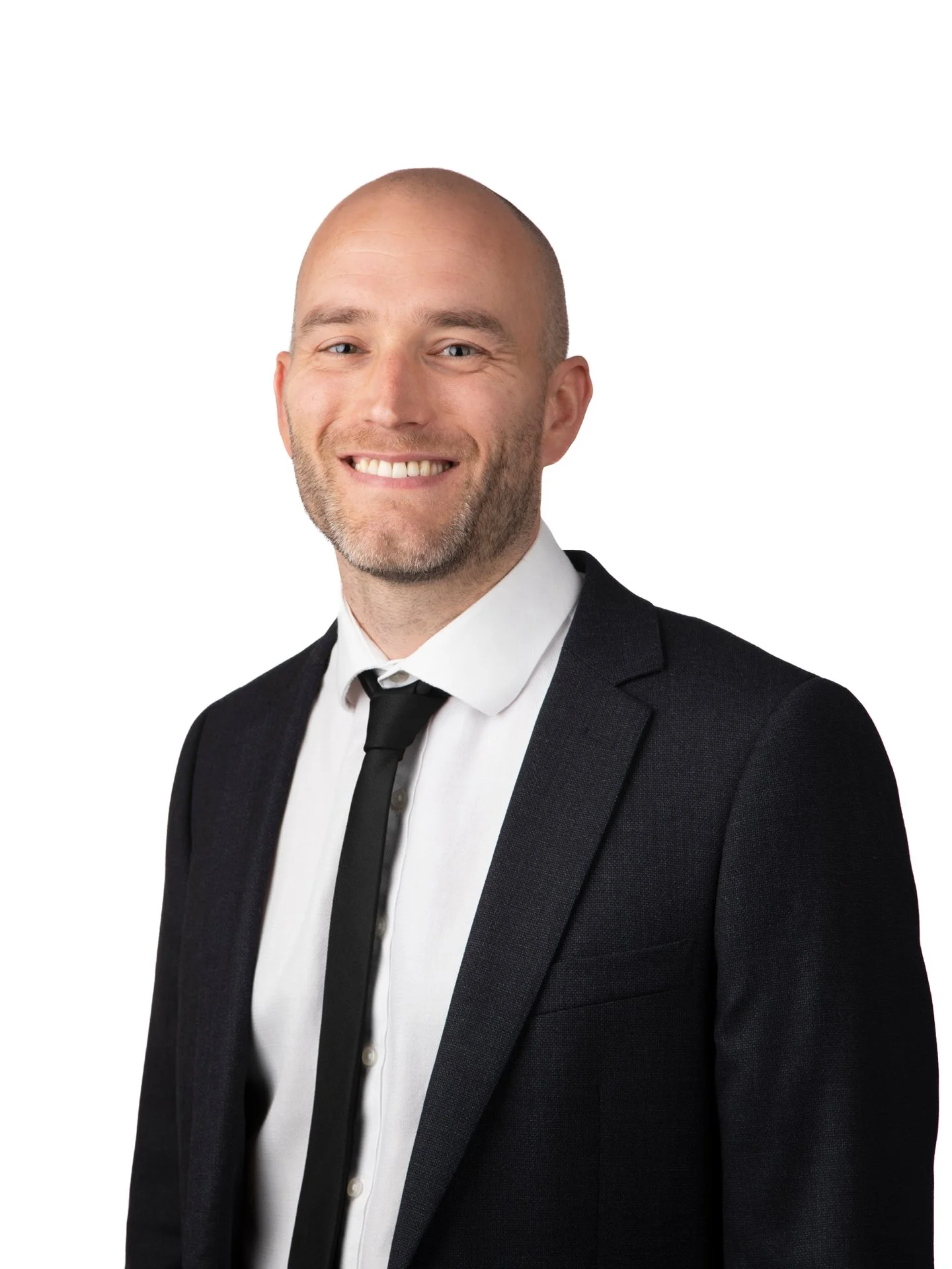 A smiling man in a black suit, white shirt, and black tie, posing against a white background.