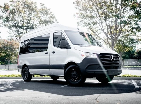White Mercedes-Benz cargo van parked in an outdoor lot with trees in the background.