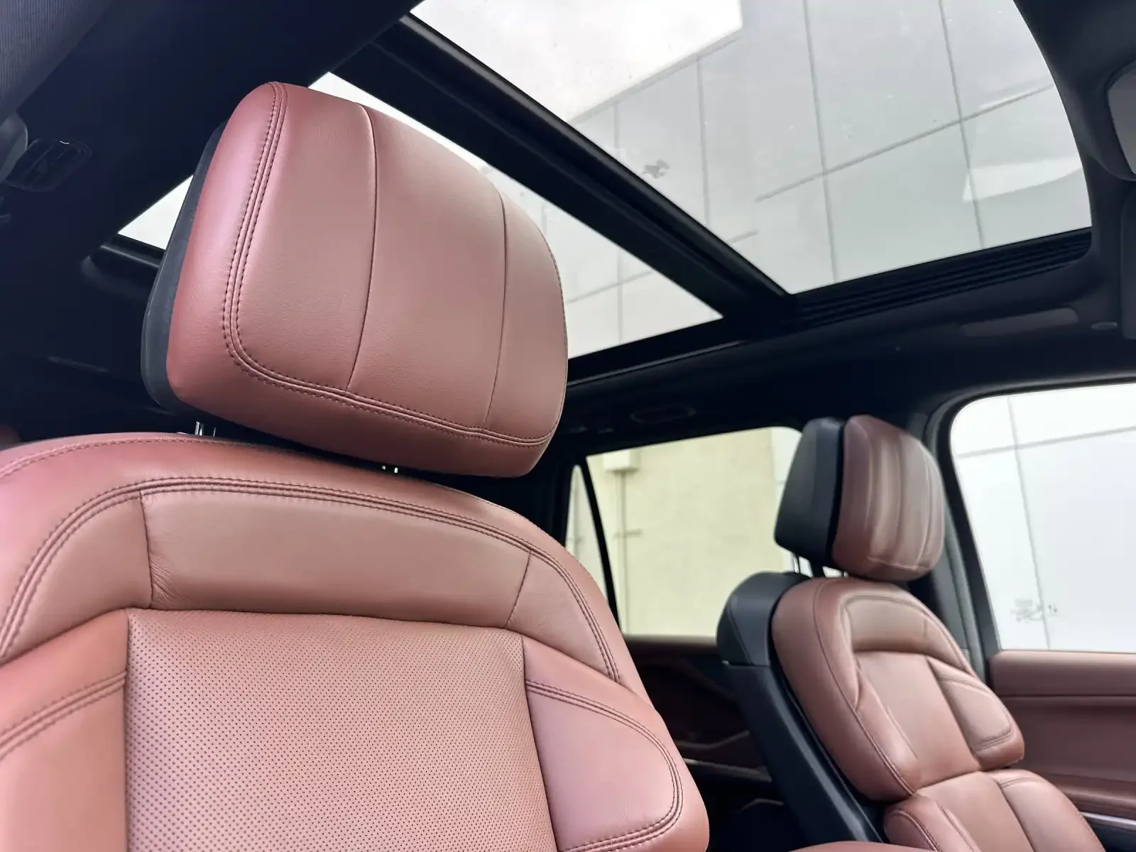 Interior of a vehicle with pink leather seats and a panoramic sunroof.