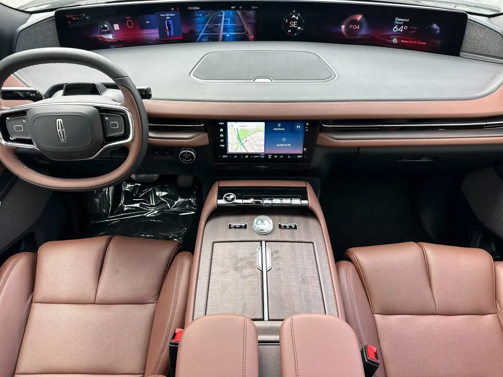 Interior view of a modern vehicle dashboard with digital displays, a steering wheel, wood and leather accents, and front seats.