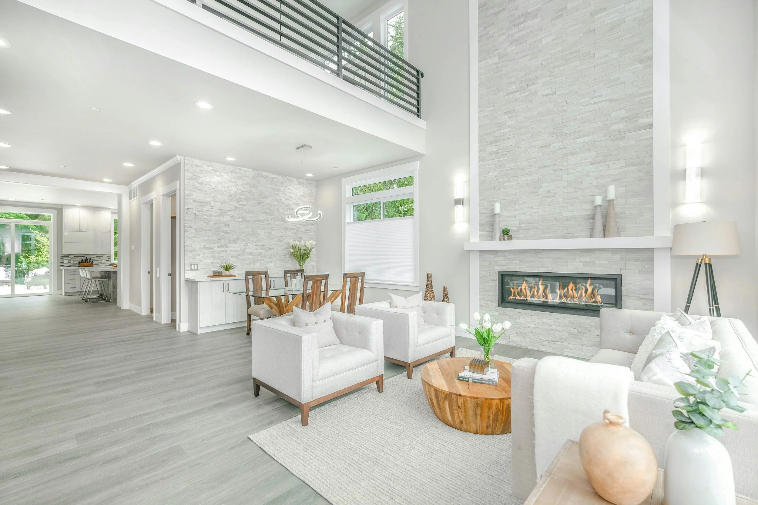 Modern living room with white walls, a stone fireplace, and large windows.