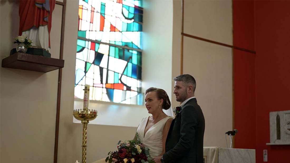  The bride and groom are beside a large stained glass window. 