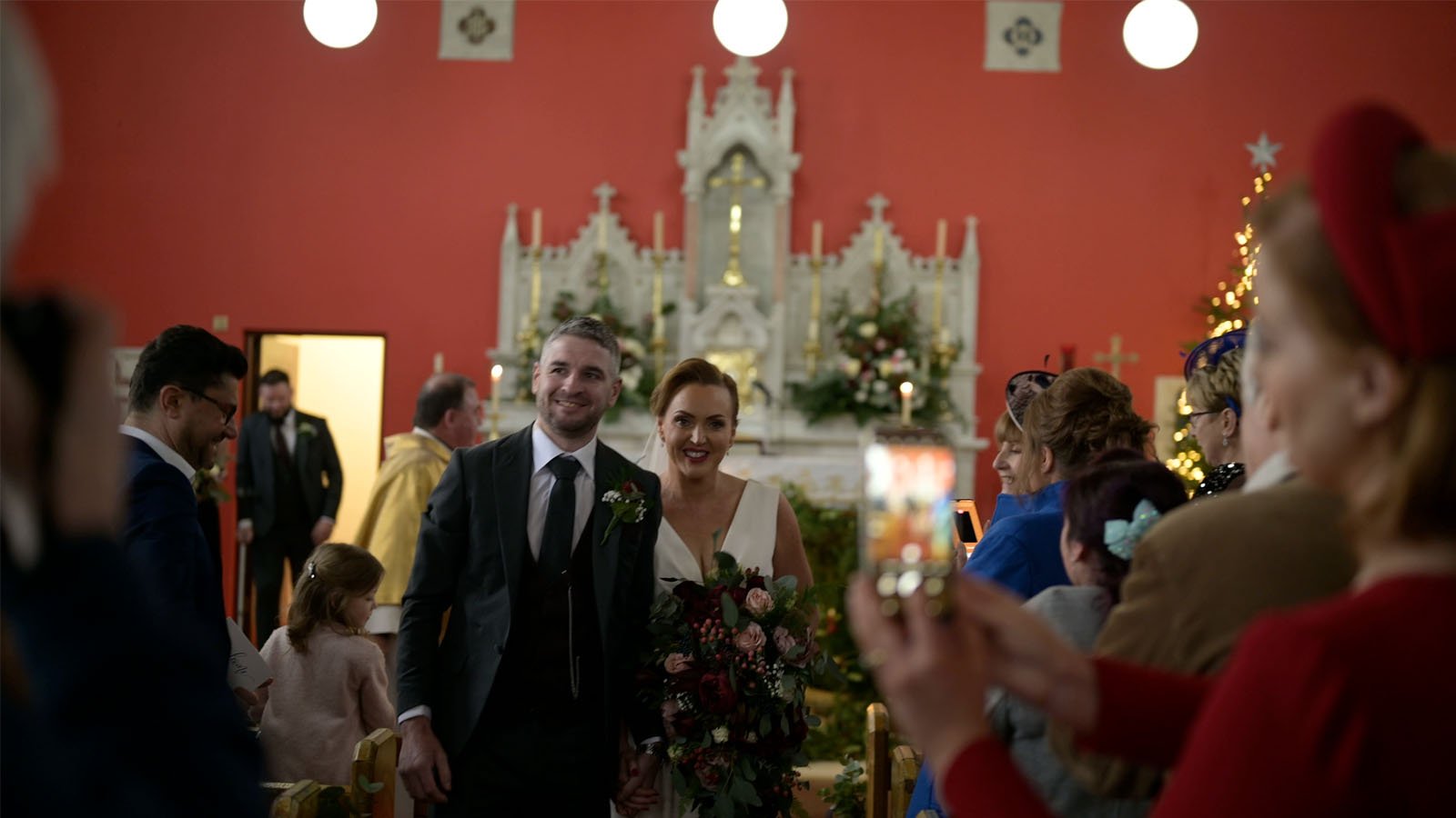  The bride and groom hold hands and walk down the aisle as guests clap. 
