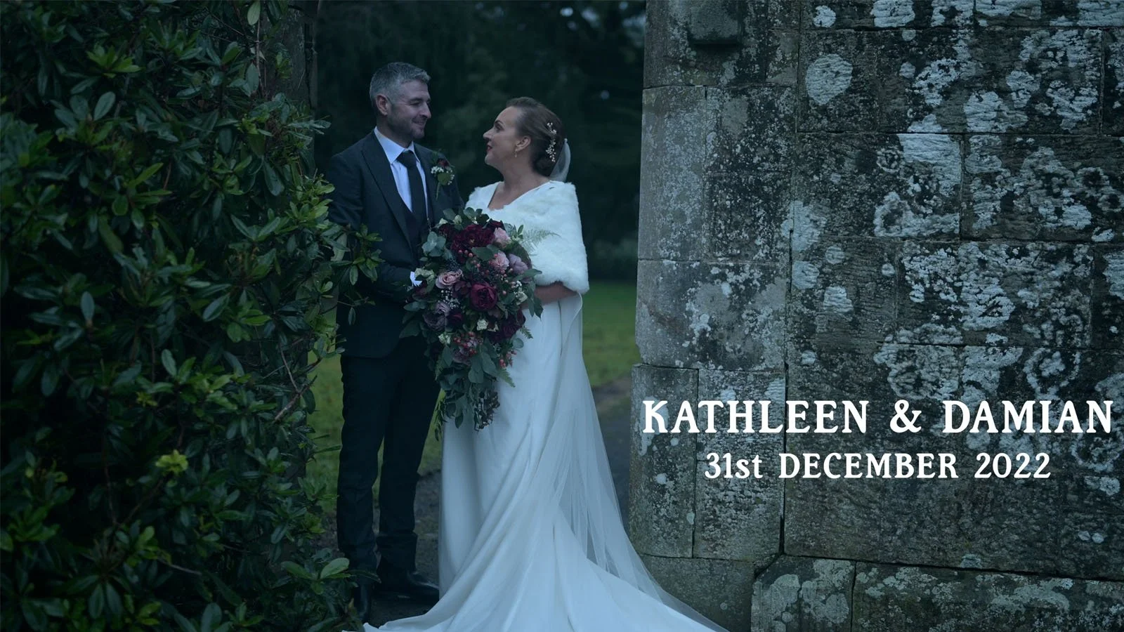  Bride with bouquet and groom beside an old stone wall. 