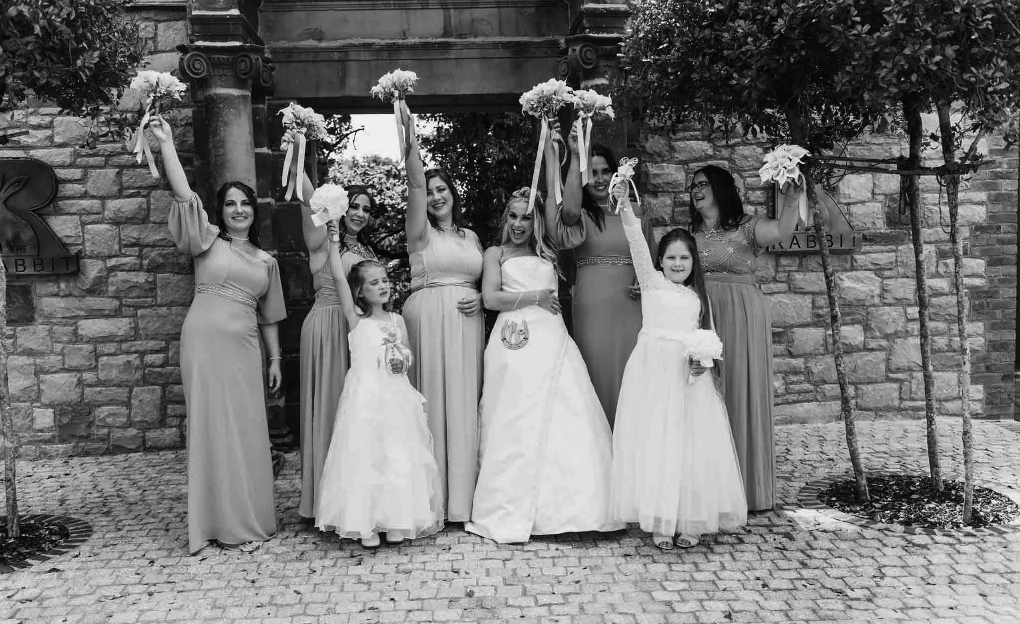Bridel with bridal part with bouquets up in the air as she had some Frequently Asked Questions for her wedding photography.