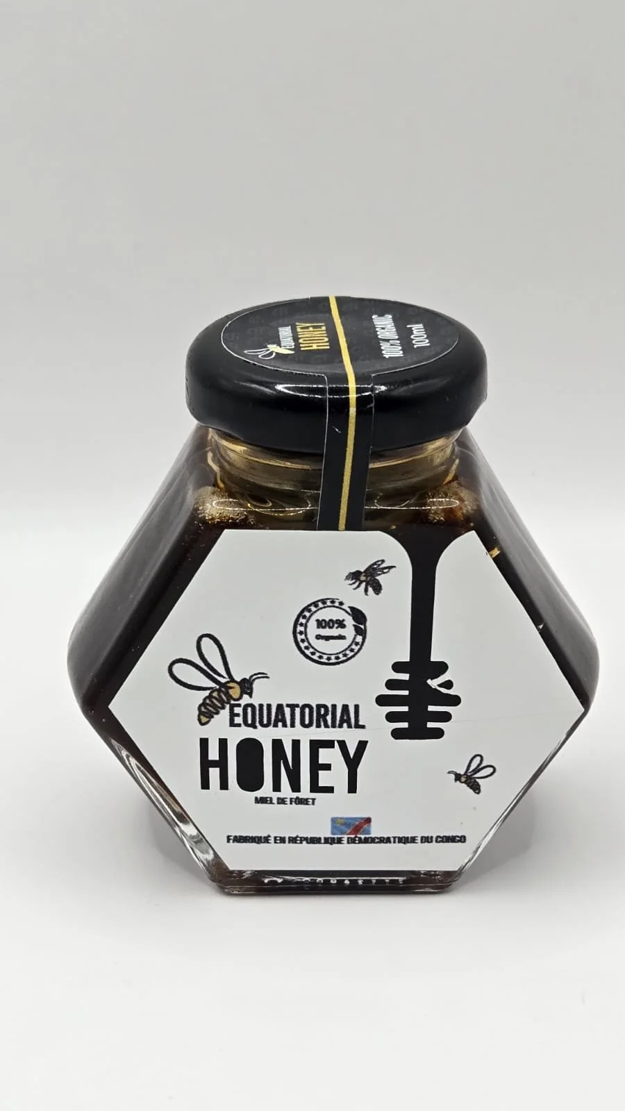 A glass jar of honey with a white label featuring bees and a honey dipper, labeled 'Equatorial Honey,' with a black lid and minimalistic design.