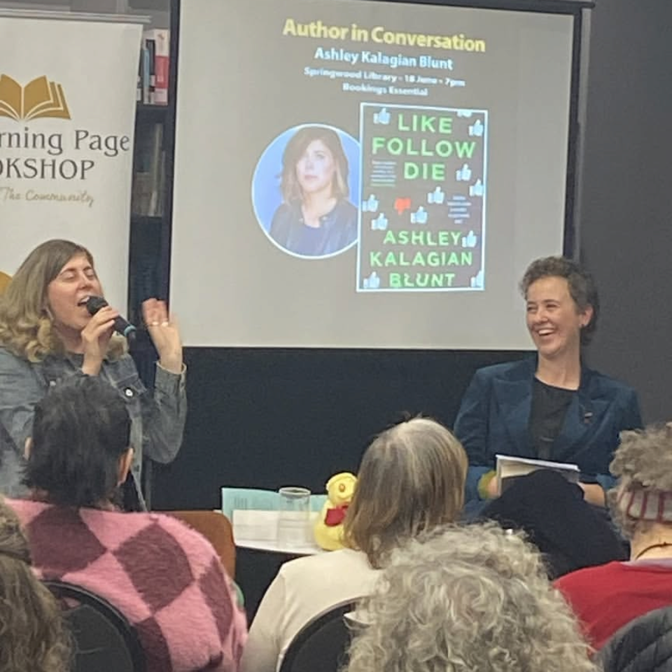Author Ashley Kalagian Blunt speaking at a book event, with a projected presentation slide showing her book cover titled "Like Follow Die" and a photo of the author.