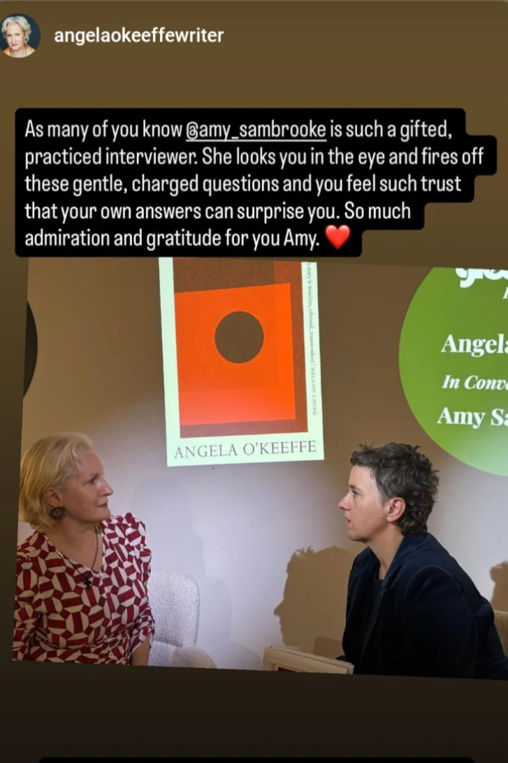Photo of two women seated facing each other, engaged in conversation. A large screen behind them displays a book cover titled 'Angela O'Keeffe' and a quote about Amy Sambrooke, who is mentioned as a gifted interviewer.