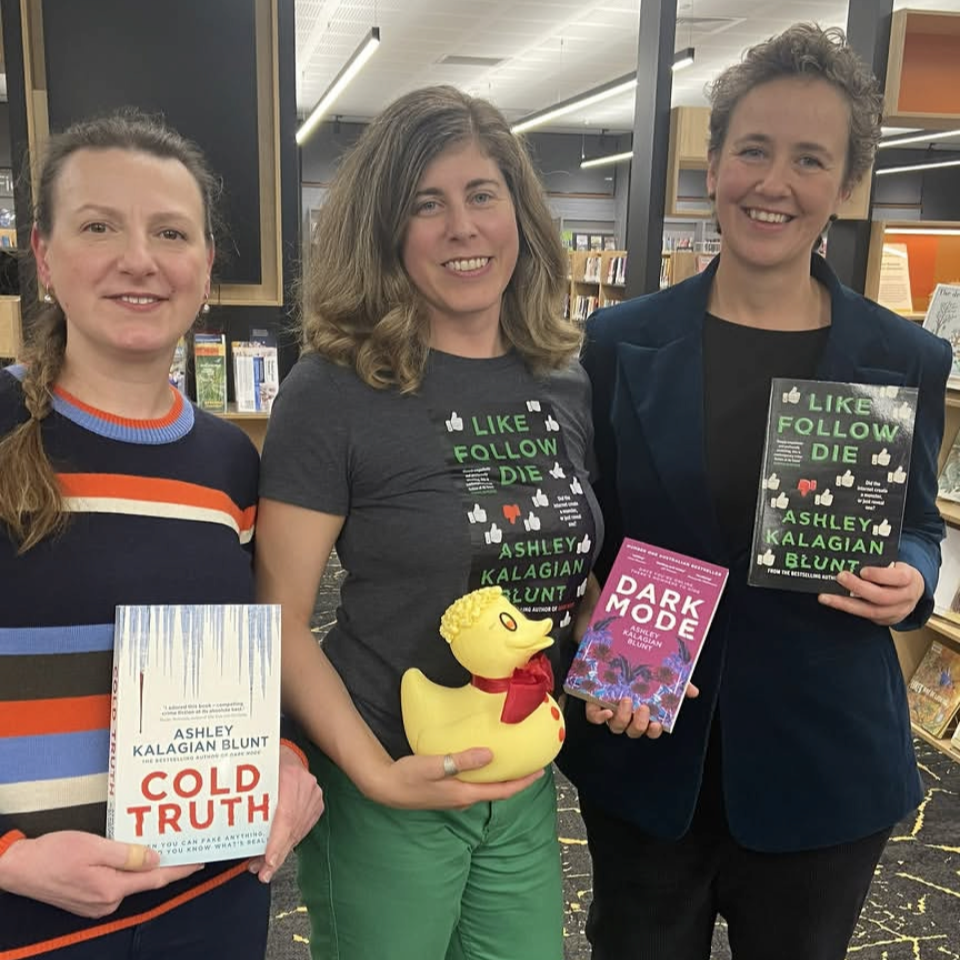 Three women standing in a bookstore, holding books by Ashley Kalagian Blunt, with one woman holding a rubber duck with a red scarf.