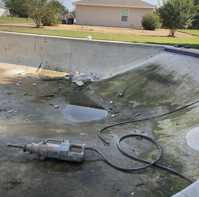 dry empty backyard pool with cracked concrete shell lifting upward