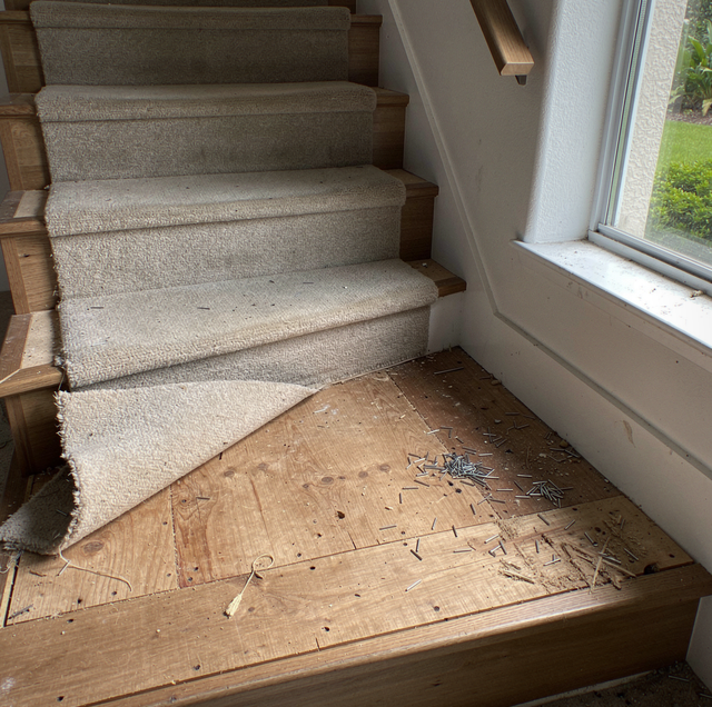 Stairs with tan carpet meeting a wooden floor landing next to a window overlooking grass.