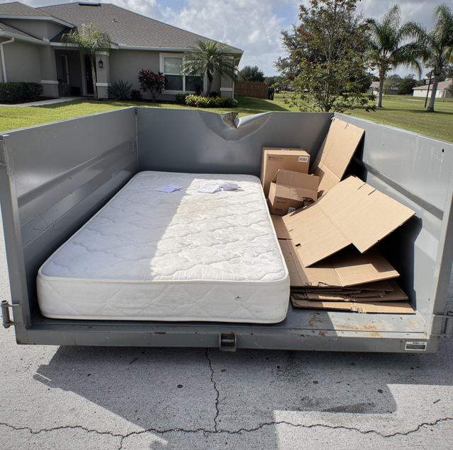 discarded mattress leaning against a full dumpster