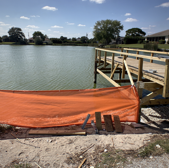 two workers dismantling wooden dock over clear lake
