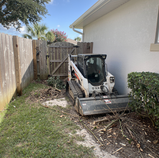 compact utility loader clearing brush beside narrow fence gate