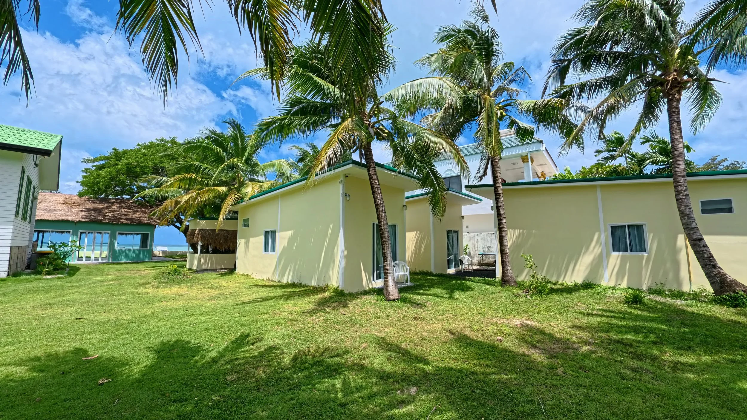 Yellow and white houses with palm trees in front, green lawn, blue sky with clouds.