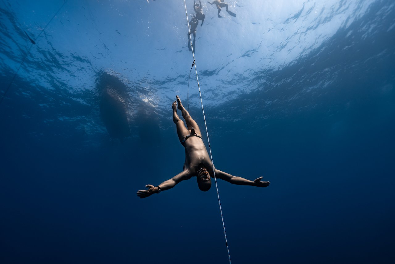 A man in swimwear hanging onto a rope underwater, with others in the background holding onto the same rope.