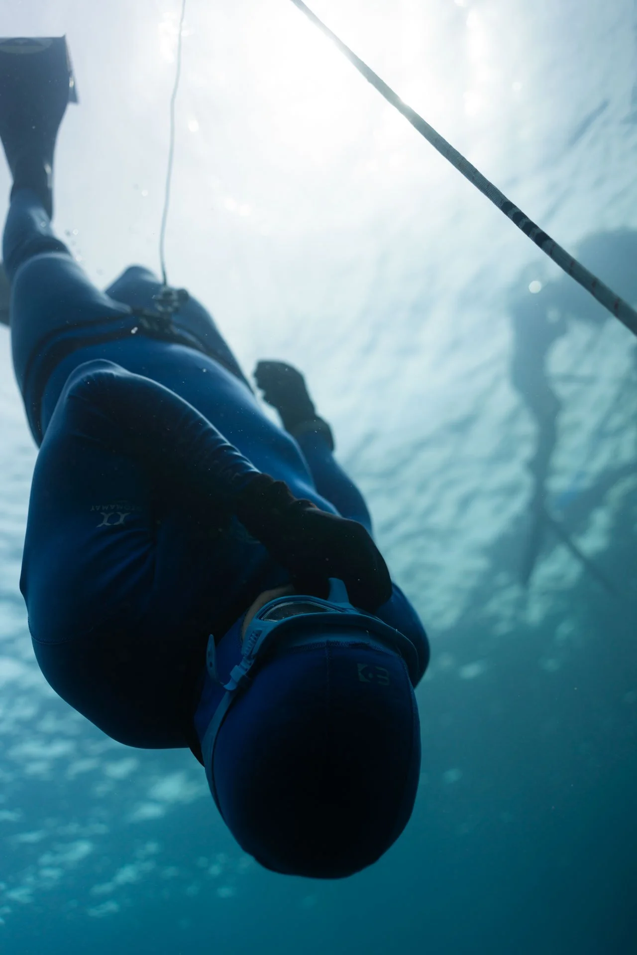 Underwater view of a person with a wetsuit, holding a fishing rod, with sunlight filtering through the water.
