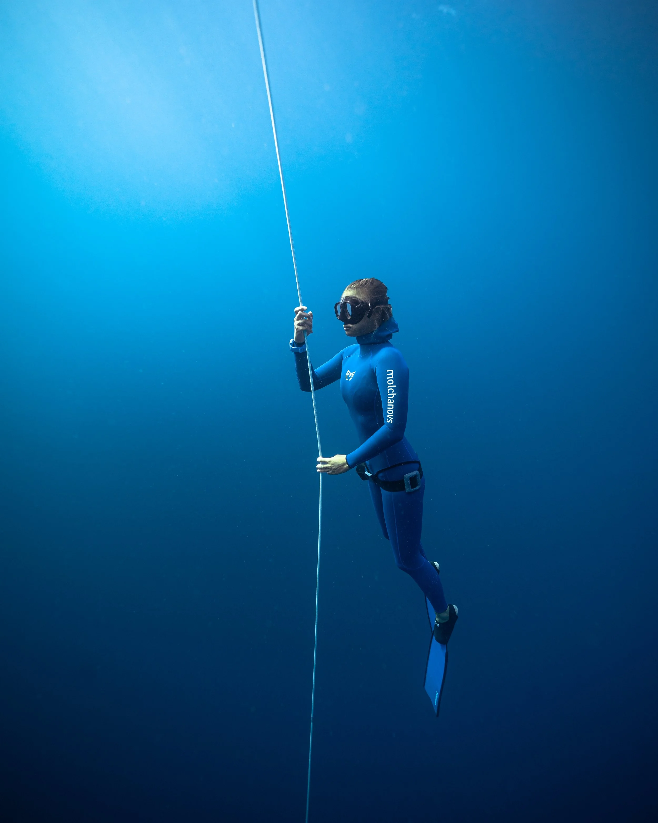 A diver wearing a wetsuit, mask, and fins swimming underwater in the ocean, surrounded by blue water and bubbles.