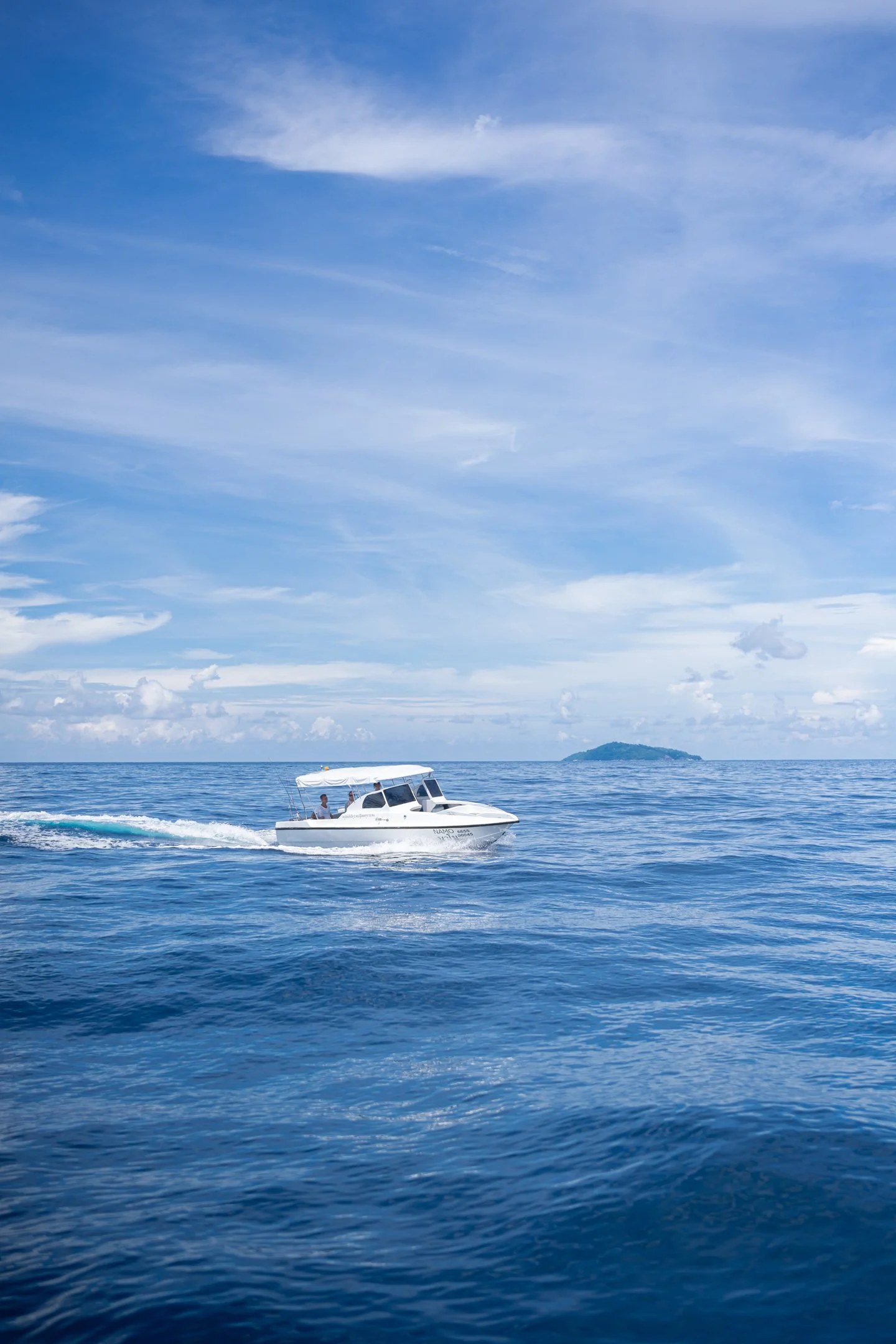 A white motorboat moving across the calm ocean waters under a partly cloudy sky with a small island in the distance.