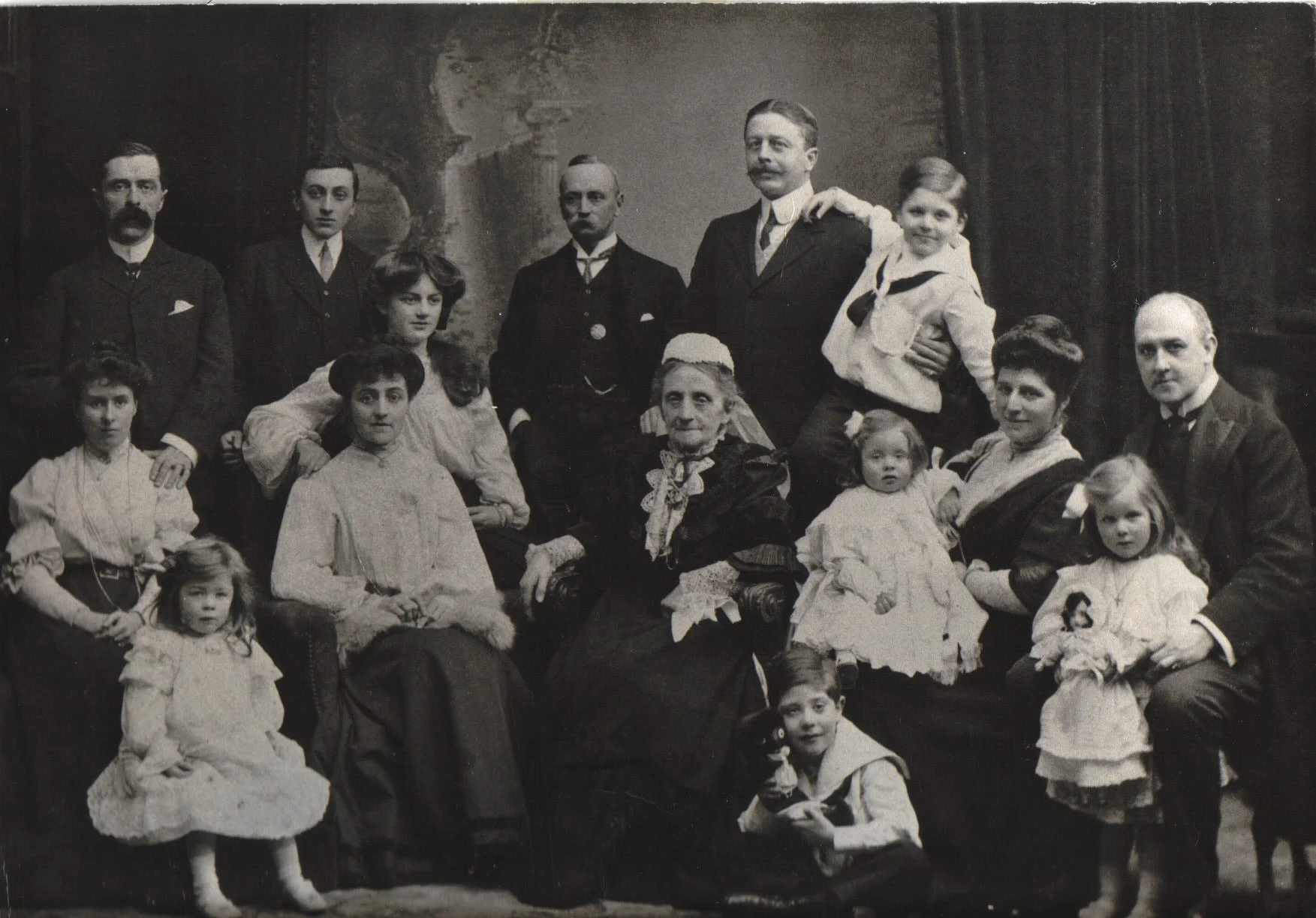 Black and white photograph of a large family group posed together, including men, women, and children, with a painted backdrop in the background.