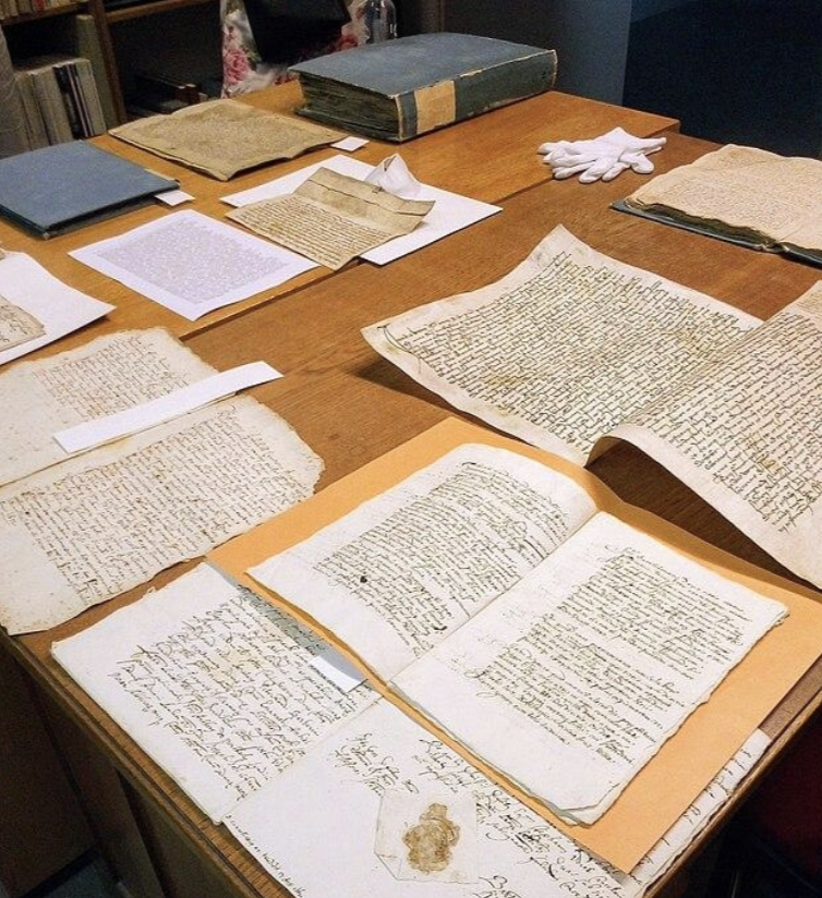Ancient handwritten documents and manuscripts spread out on a wooden table.