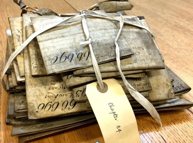 A bundle of old, handwritten documents tied with a ribbon, with a beige tag that reads "Electric 84", placed on a wooden surface.