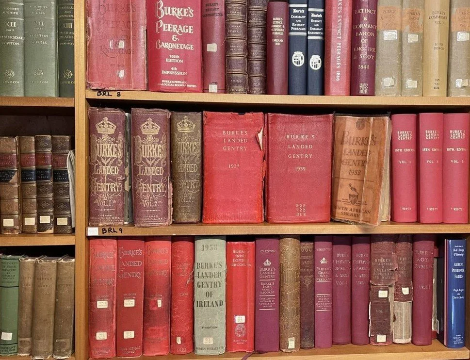 Bookshelves filled with various old and worn hardcover books, many titled 'Burke's Landed Gentry' from different years and editions.