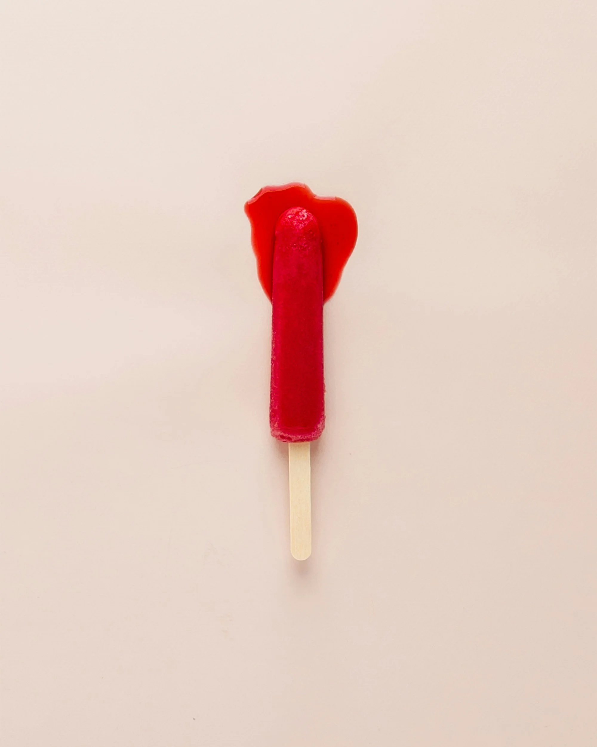 Red popsicle with a strawberry on top on a white background.