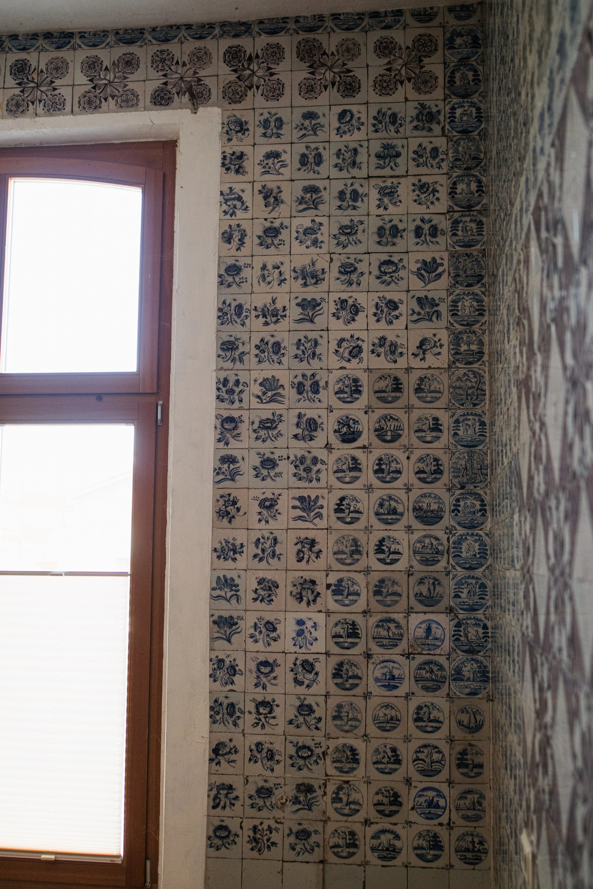 Alte Wandfliesen mit blauer und weißer Musterung, neben einem großen Fenster, in einem Raum.