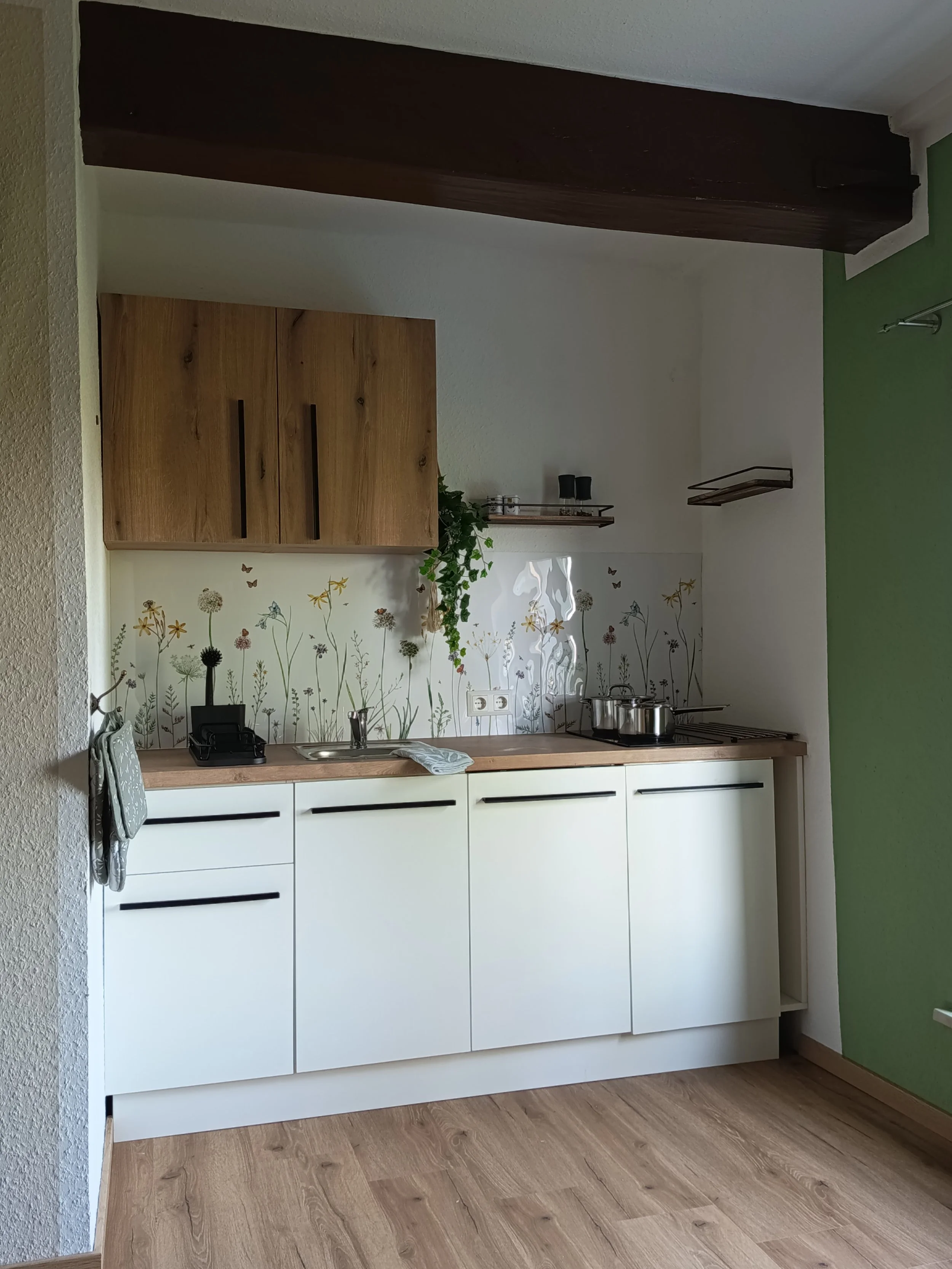 Moderne Küchenzeile mit weißen Schränken, Holzarbeitsplatte und einer stilvollen Fliesenspiegel mit Blumenmuster, in einer Ecke mit grün gesträuchtem Wandabschnitt.