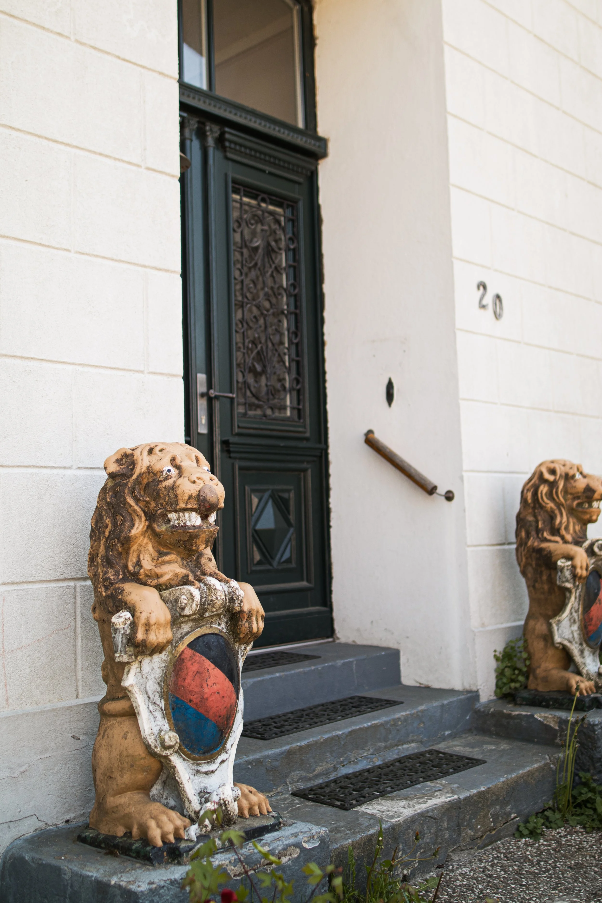 Eingang eines Hauses mit schwarzen Doppeltüren, zwei Löwenskulpturen auf den Stufen, die das Haus flankieren.