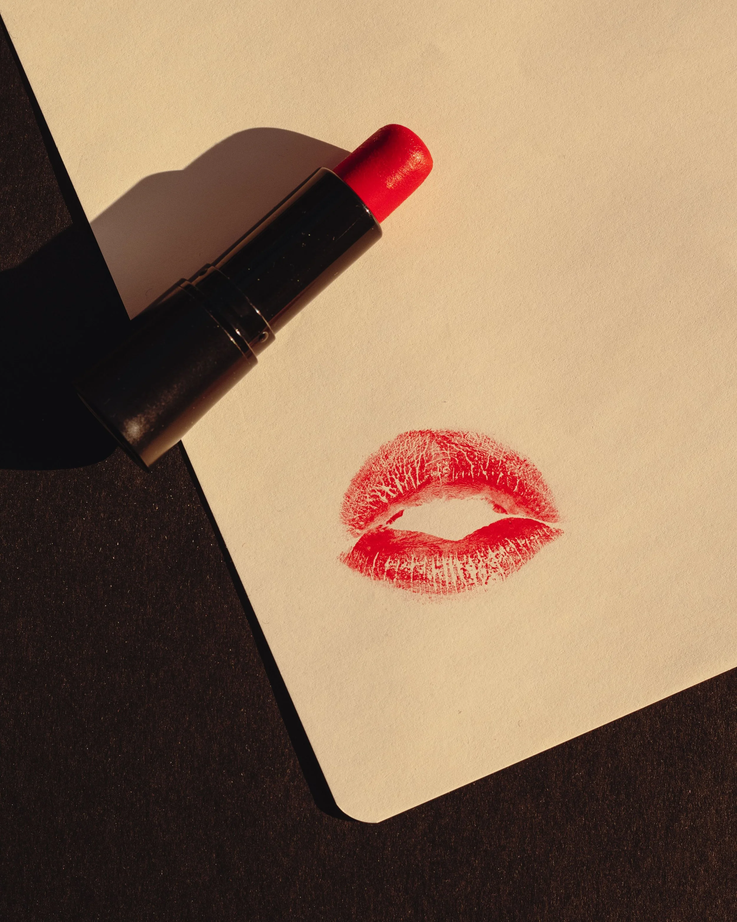 A tube of red lipstick lying on its side on a white surface, with a red lipstick kiss print below it.