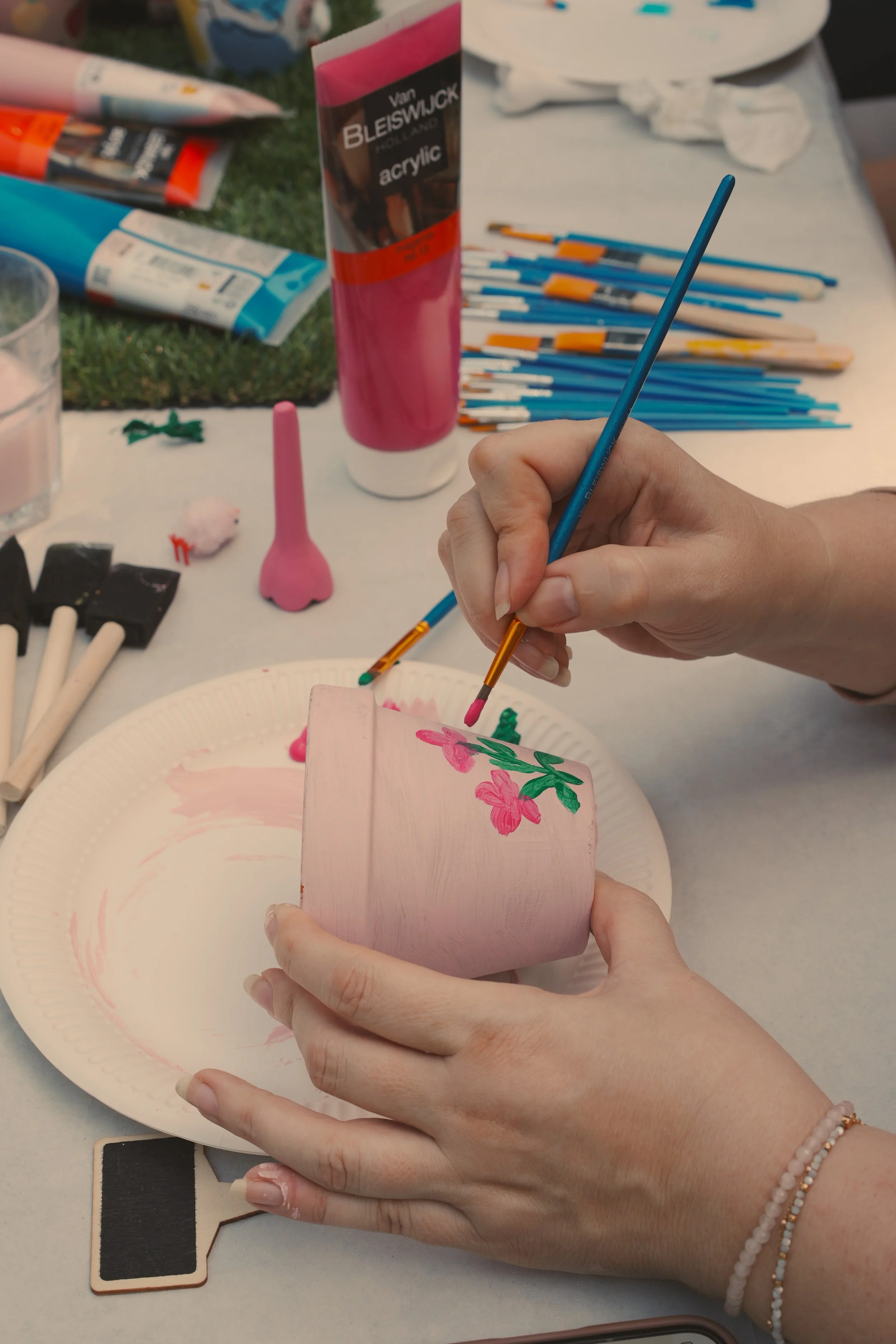 Close-up of a participant using a fine paintbrush to detail pink flowers on a terracotta pot at a retreat art workshop.