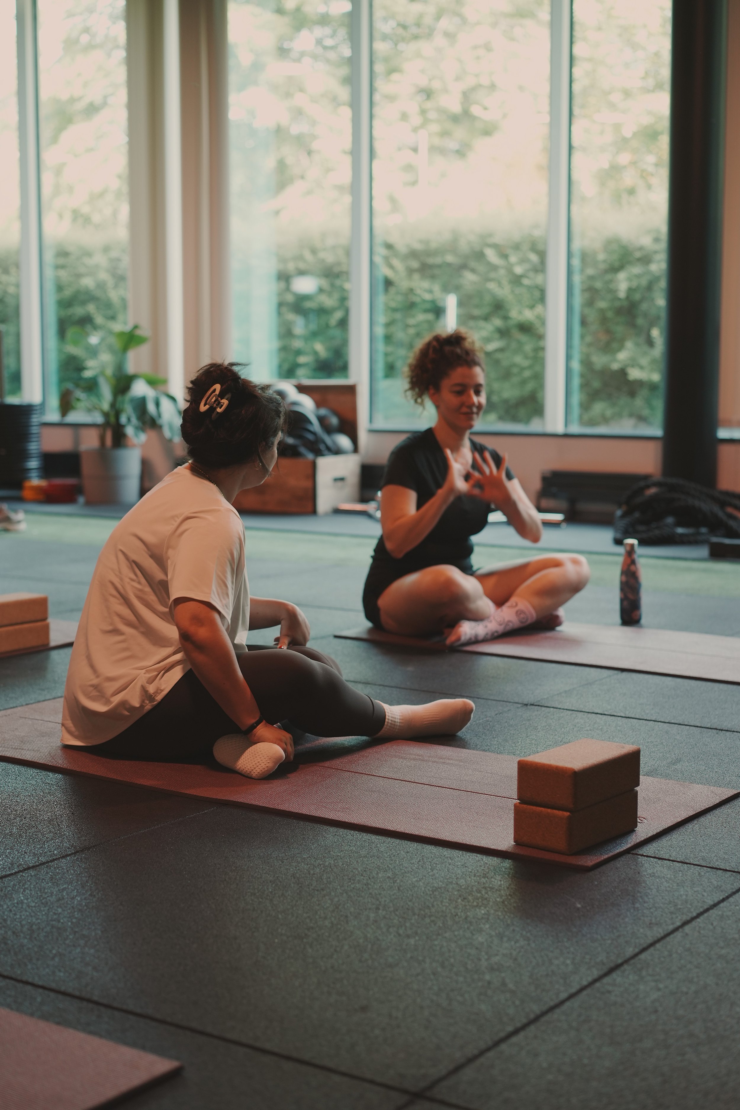 Two retreat participants sitting on yoga mats and chatting during a break at an indoor wellness retreat.