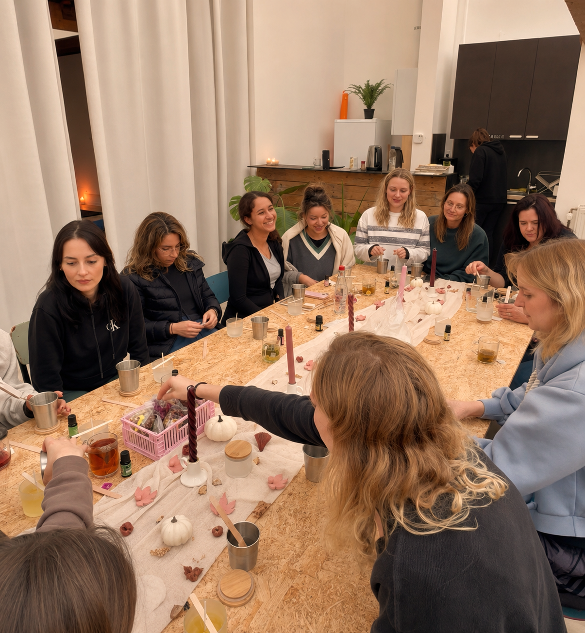 A group of women sitting around a large table crafting handmade candles during a creative workshop at a wellness retreat