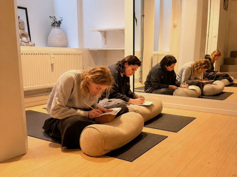 Two women sitting on yoga mats and bolster pillows journaling during a mindfulness workshop at a wellness retreat.