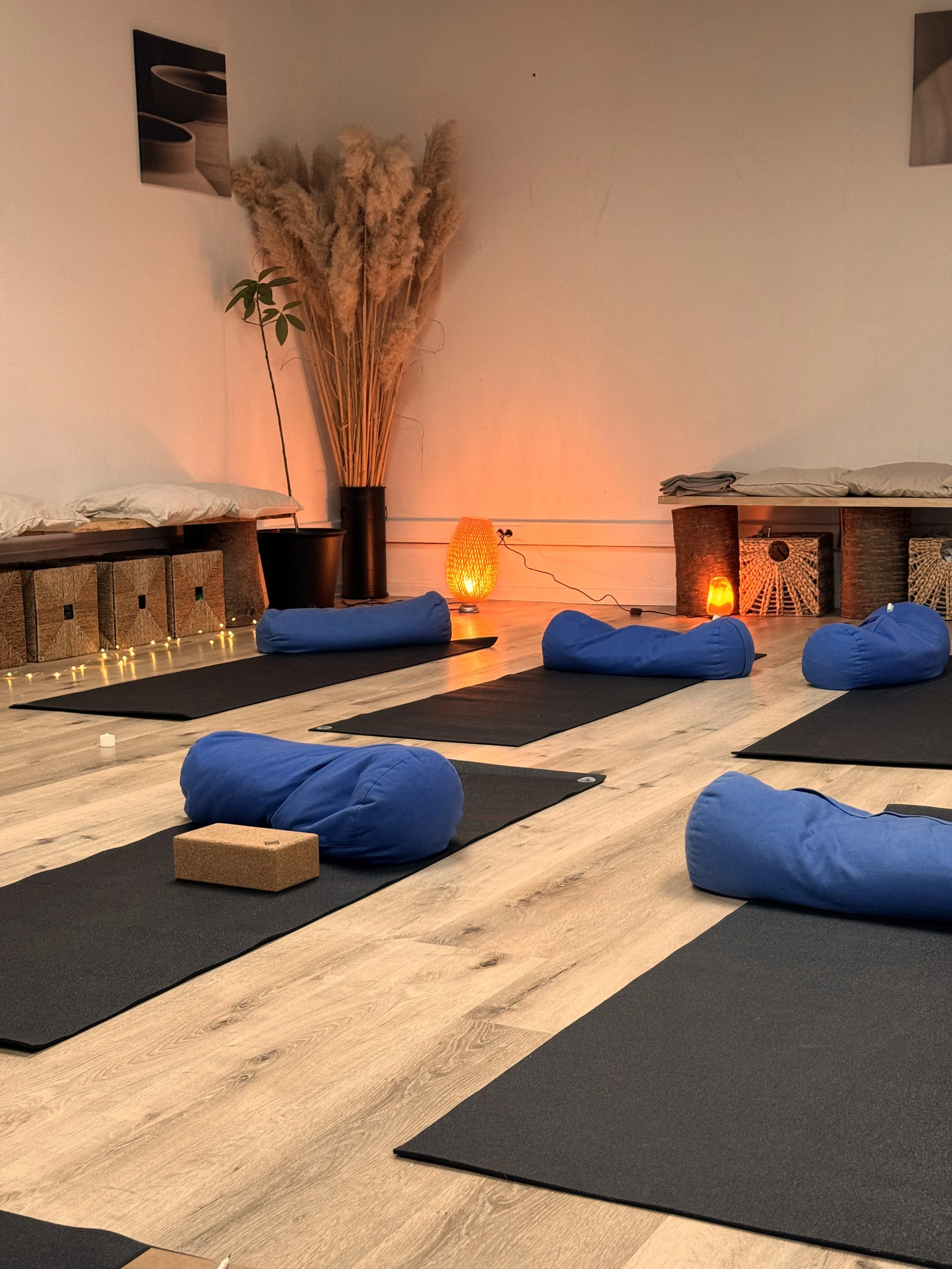 Cozy indoor yoga studio setup with black mats, blue bolsters, and warm glowing lamps for a restorative retreat class.