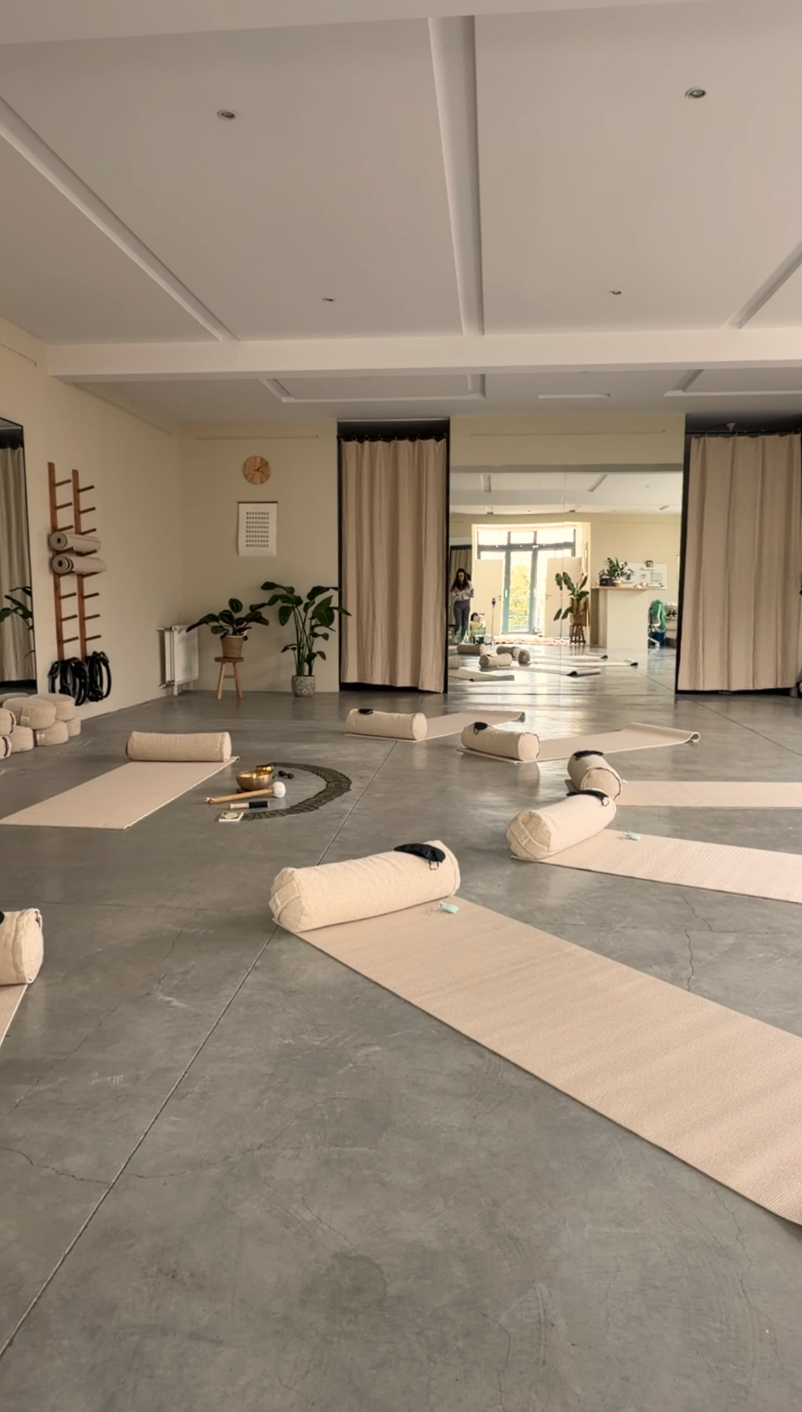 A bright, minimalist yoga studio set up with beige mats, bolsters, and a singing bowl for a sound healing retreat session.