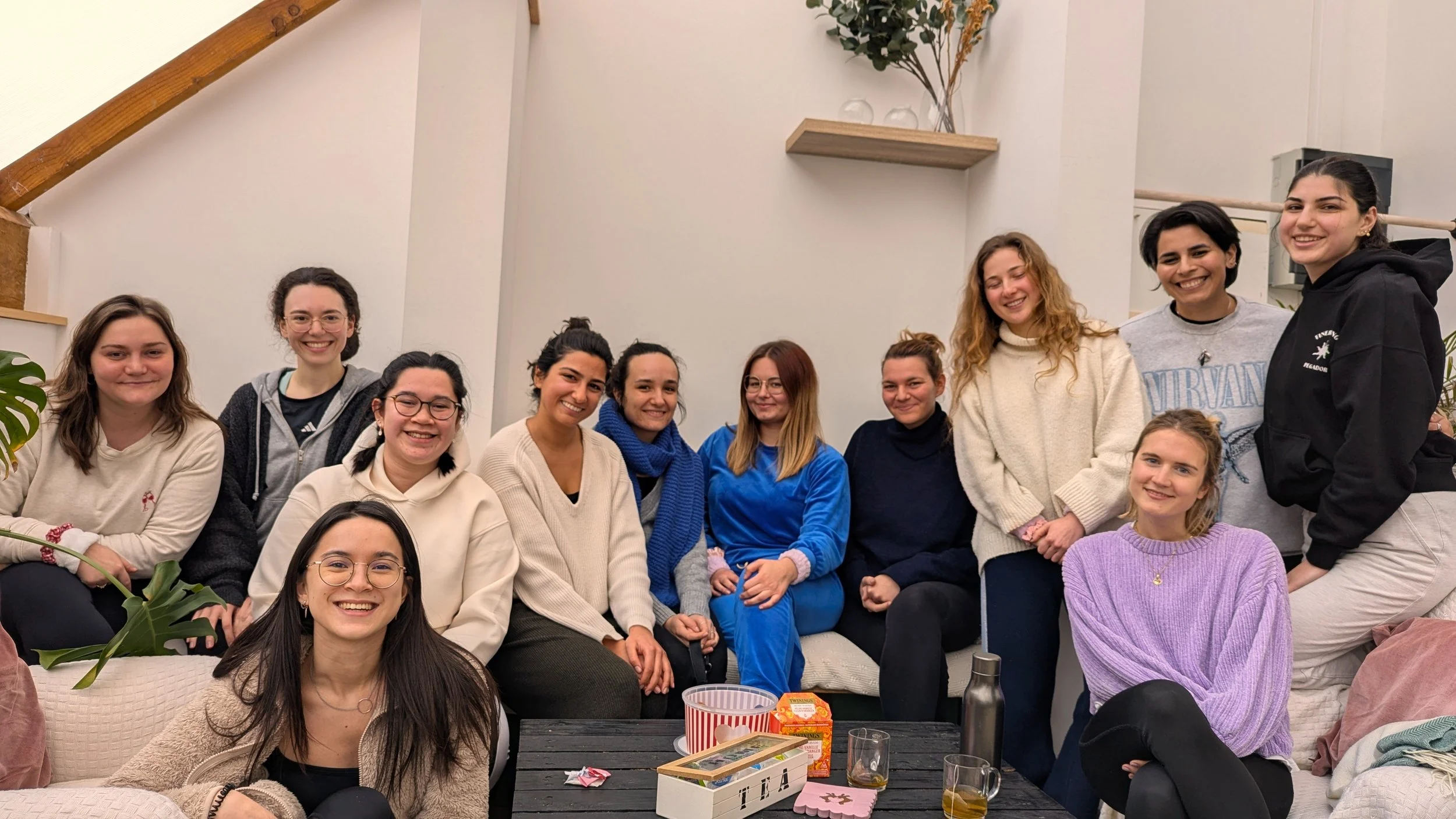 A group of eleven smiling women posing together indoors around a tea table at a cozy creative wellness retreat.