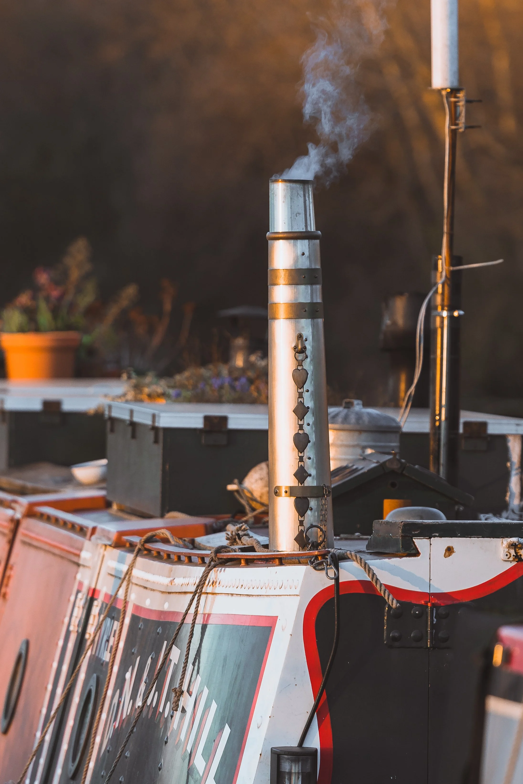 A metal pipe emitting white smoke on a flatbed truck with various objects and plants in the background.