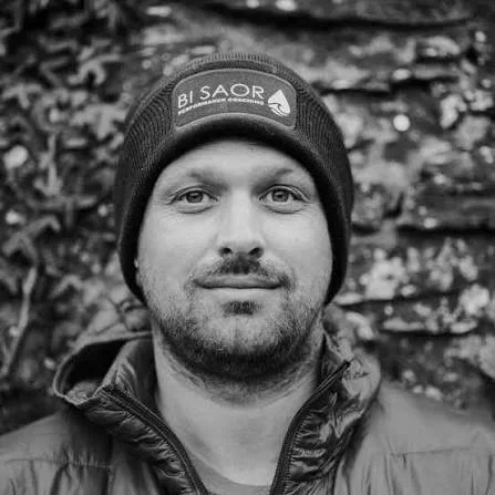 A man wearing a beanie and a jacket, outdoors with trees in the background.