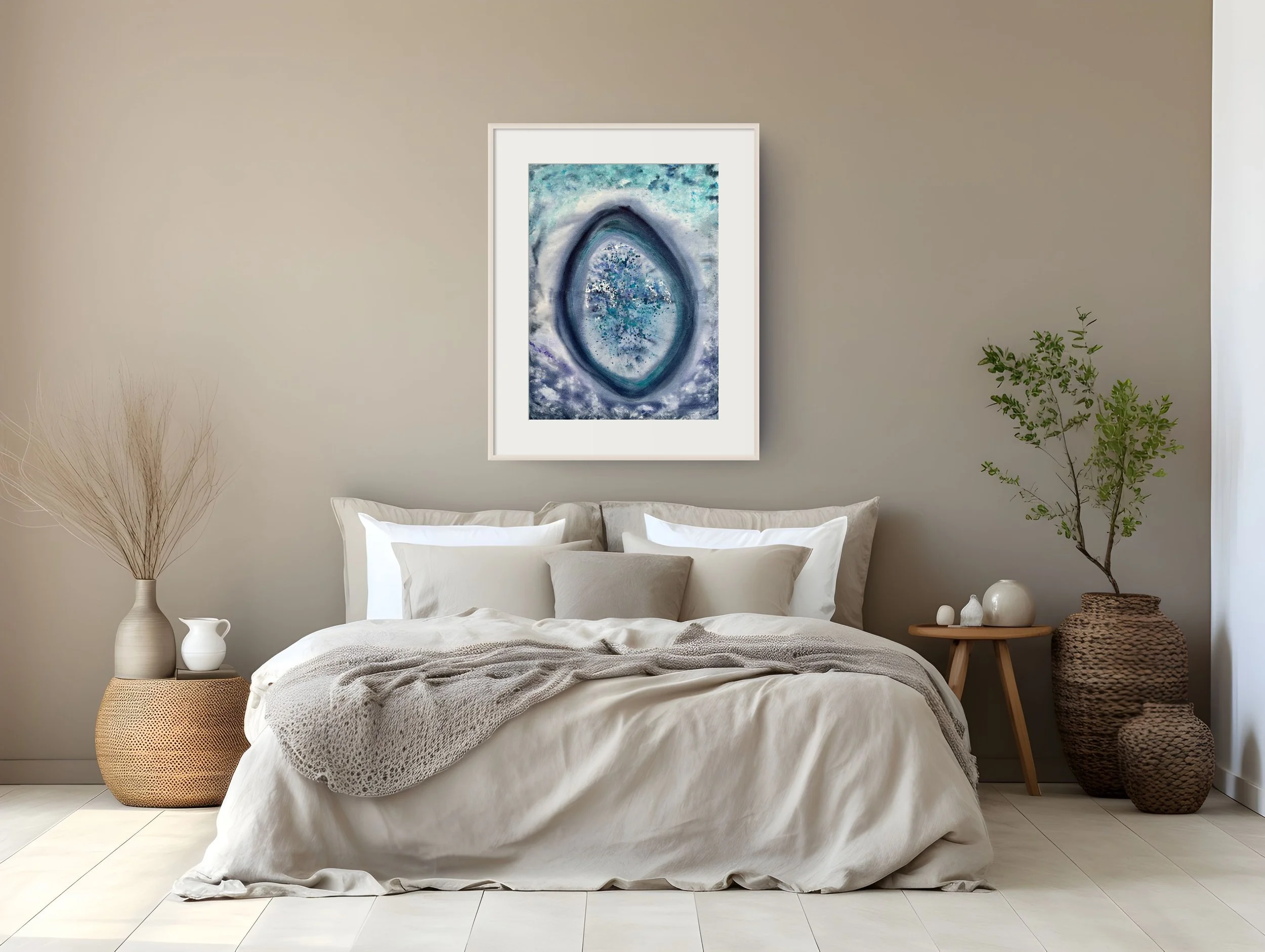 A cozy bedroom with beige walls, a bed with white linens and multiple pillows, a large abstract blue and white artwork above the bed, two vases on a side table to the left, a book and a vase on a small wooden table to the right, and a potted plant in the corner.