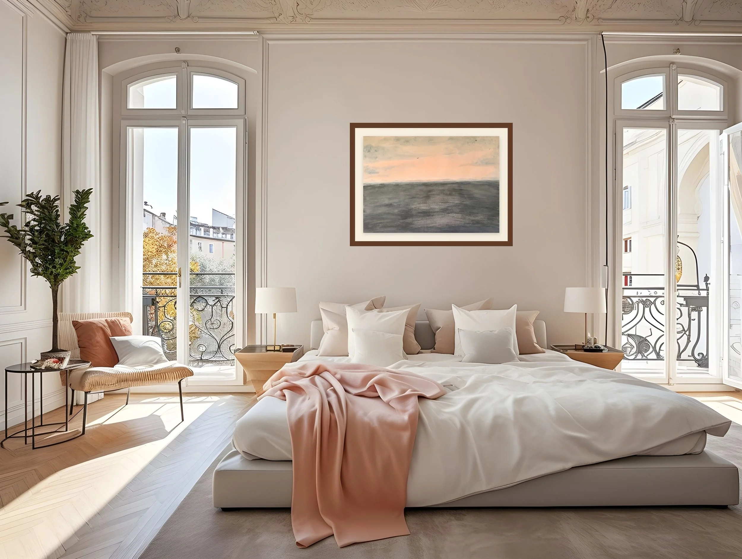 A bright and airy living room with tall windows and French doors, white walls, a white sofa with beige and pink cushions, a wooden side table with lamps, a painting on the wall, a potted plant, and a balcony view of buildings and trees.